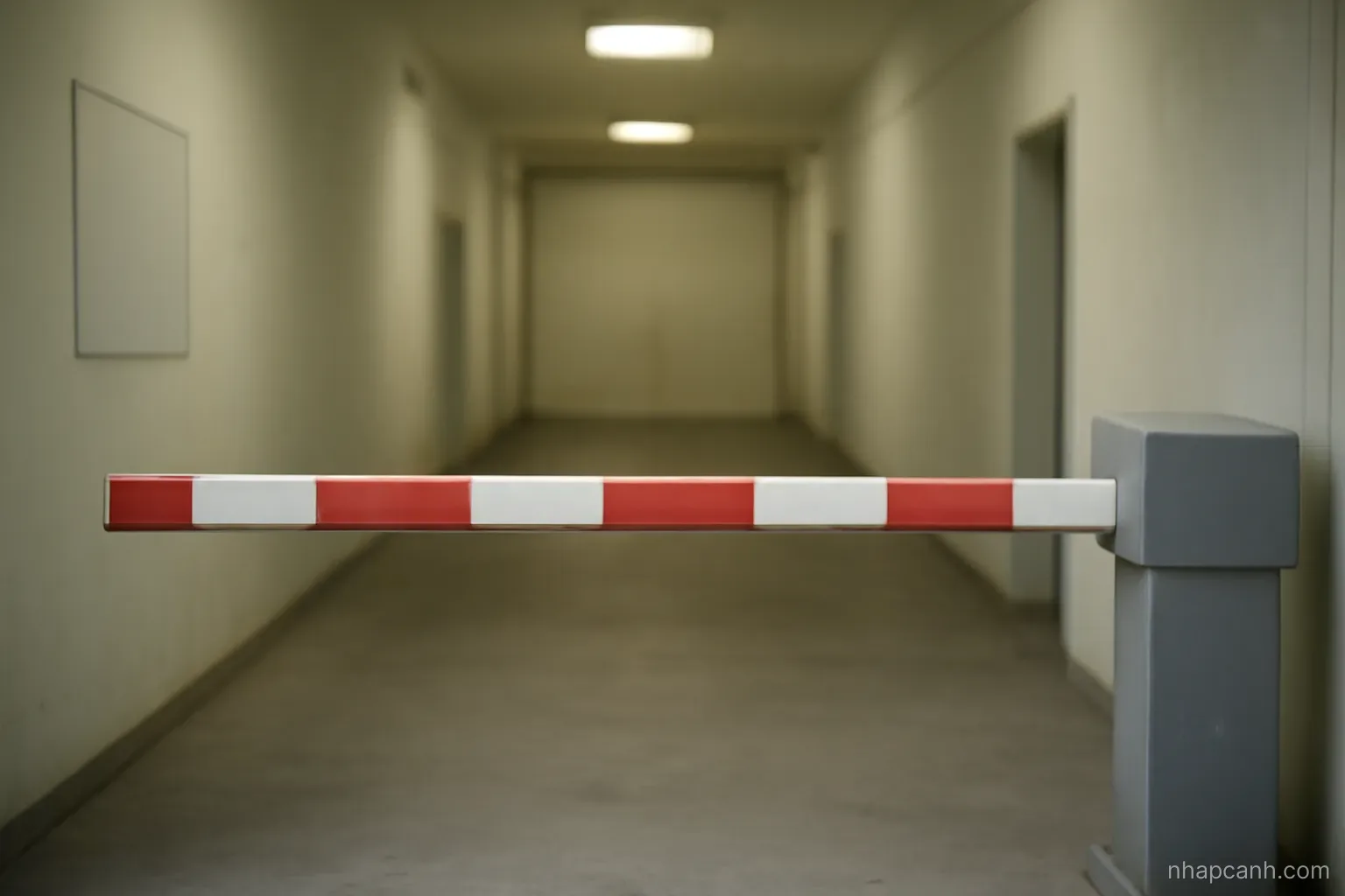 a closed barrier gate at an empty checkpoint corridor with a red and white bar lowered, plain walls, even lighting, no text