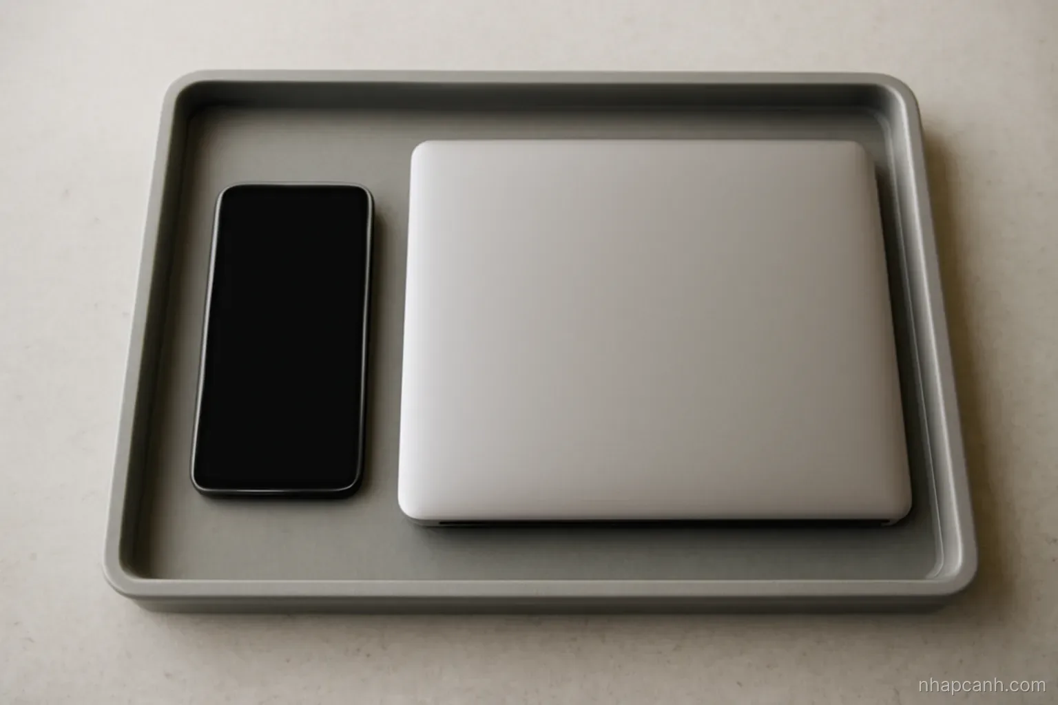 a switched off smartphone and a closed laptop resting in a grey tray on an inspection counter, top down view, screens blank